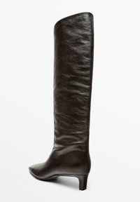 Hnědá kožená vysoká bota po kolena s špičatou špičkou a nízkým, čtvercovým podpatkem. Povrch má texturovaný vzhled s jemnými vráskami.
