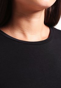 Maglietta nera a girocollo realizzata in un tessuto leggero e liscio con un design aderente. Dettaglio in primo piano del collo e delle finiture.