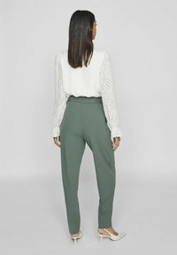 Green tapered trousers with a smooth texture, paired with a white blouse featuring a wave pattern and puffed sleeves.