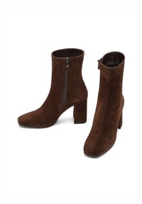 Botas de tobillo de ante marrón con punta cuadrada, tacón bloque y cremallera lateral. Presenta una textura suave y una silueta ajustada.