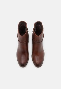 Bottines en cuir brun avec une texture lisse, bout arrondi et fermetures éclair sur les côtés. Présentant un talon bas et un design simple.