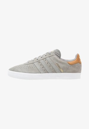Le sneakers basse in suede grigio presentano tre strisce diagonali, dettagli perforati, una punta testurizzata e un accento in pelle marrone sulla parte posteriore.