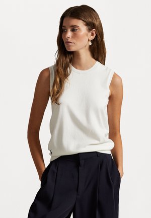 Top sin mangas en color crema, hecho de un tejido suave con un escote redondo, combinado con pantalones oscuros de color marino; presenta un diseño minimalista y una sutil marca.