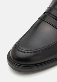 Black leather shoe with a smooth finish, rounded toe, and layered design featuring visible stitching and a secure rubber sole.