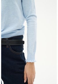 Light blue long-sleeve sweater with textured fabric and ruffled cuffs, paired with dark blue jeans and a black leather belt with gold accents.