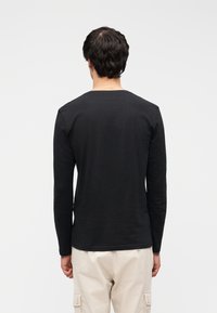 Bluza neagră cu mâneci lungi, realizată din bumbac, cu guler rotund, având o textură netedă și un croi mulat.