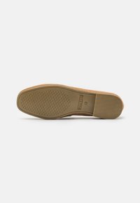 Semelle de chaussure en daim beige avec un motif antidérapant texturé. Présente un bout arrondi et une étiquette latérale, mettant en avant une construction en caoutchouc durable.