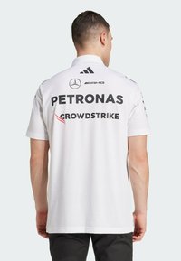 White sports polo shirt featuring black logos, including "PETRONAS" and "CROWDSTRIKE," with short sleeves and a classic collar design.