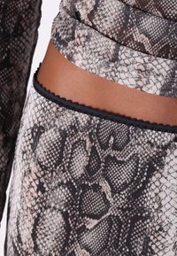 Tecido com padrão de pele de cobra nas tonalidades de preto, bege e rosa. Superfície texturizada e acabamento em preto com bordas onduladas na bainha.