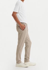 Beiga bomullbyxor med smal passform, sidofickor och en baketikett. Kombineras med en kortärmad vit t-shirt och vita sneakers.