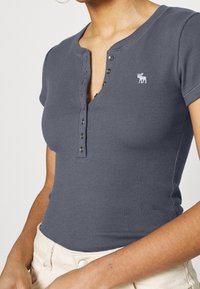 Grå ribbad kortärmad skjorta med knapp-up henley-nacke och en liten broderad logotyp. Har en figurnära design och mjuk textur.