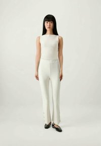 Hvit stripete tanktopp med tettsittende hvite bukser, utsvingt nederst, med knappdetaljer, vist på en modell mot en nøytral bakgrunn.