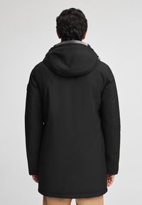 Parka nera con cappuccio, caratterizzata da un tessuto liscio e opaco, maniche lunghe e un taglio di media lunghezza. Senza loghi o dettagli visibili.