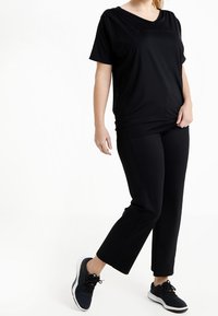 Black short-sleeve top with a rounded neckline, paired with black ankle-length pants. Model wears dark athletic shoes. Plain design.