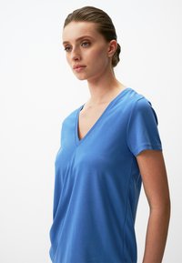 Niebieska koszulka z krótkim rękawem w serek, wykonana z miękkiego materiału o gładkiej strukturze, z delikatnymi bocznymi szwami i luźnym krojem.