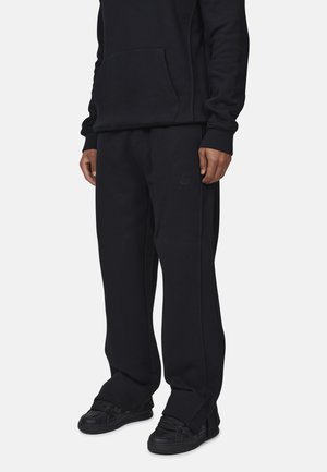 Felpa nera in misto cotone con tasca frontale, abbinata a pantaloni in pile neri coordinati. Entrambi hanno una vestibilità comoda e un branding discreto.