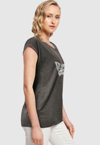 Grå t-shirt med korte ærmer, V-hals og sommerfugle grafik. Tøjet har en blød tekstur; afslappet pasform, parret med hvide bukser.