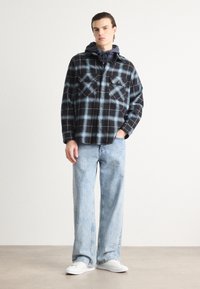 Svart och ljusblå rutiga skjortan med två bröstfickor, knappdesign, bärs över en marinblå hoodie, i kombination med ljusa vida jeans och vita sneakers.