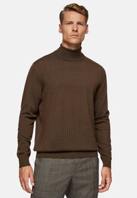 Brown turtleneck sweater in a ribbed texture with long sleeves and a fitted silhouette, paired with gray checked trousers.