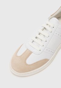 Weiße Sneaker mit einem beigen Wildlederakzent, runder Spitze, flacher Schnürung und perforierten Details an den Seiten. Gummisohle.