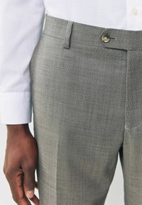 Gray tailored pants with a textured fabric, featuring a single button closure and belt loops, paired with a white dress shirt sleeve.