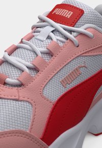 Αθλητικά παπούτσια Puma με λευκό επάνω μέρος από δίχτυ, ροζ και κόκκινες δερμάτινες λεπτομέρειες, χοντρά λευκά κορδόνια και κόκκινη ετικέτα με λογότυπο στη γλώσσα.