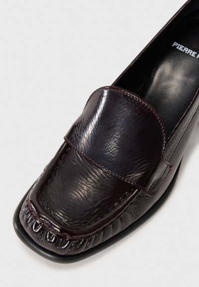 Burgundske usnjene loafer čevlje s teksturirano površino, ki imajo zaobljen toe in stikane detajle vzdolž vamp in podplata.