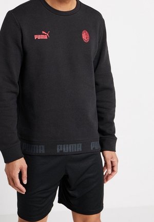 Schwarzer Puma-Sweatshirt mit roten Logos und passenden schwarzen Shorts, getragen von einer Person vor einem schlichten weißen Hintergrund.