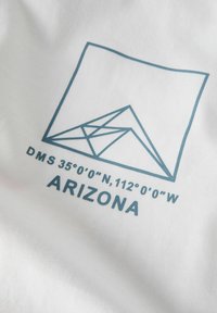 Tissu blanc avec un motif géométrique bleu et du texte : "DMS 35°00'00" N, 112°00'00" W" et "ARIZONA" en lettres gras.