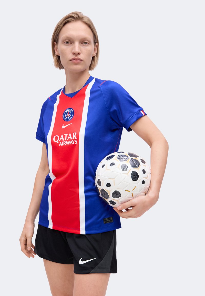 Femme en maillot de football du Paris Saint-Germain tenant un ballon de football blanc et noir à motifs, portant un short noir Nike.