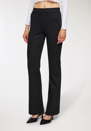 Pantaloni a righe nere con design svasato, in tessuto liscio e con cintura elastica. Abbinati a tacchi slingback neri a punta.