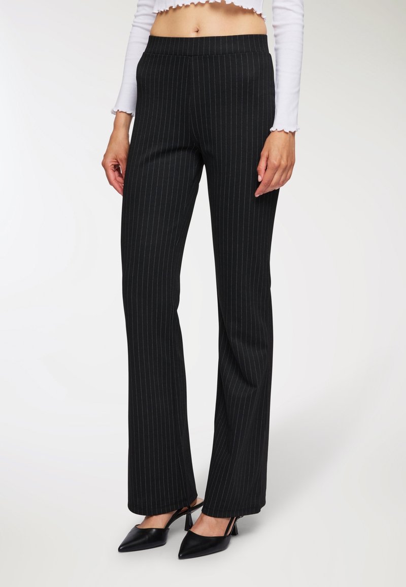 Czarne spodnie w prążki z rozszerzanym krojem, gładki materiał i elastyczna talia. Połączone z czarnymi szpilkami z odkrytymi piętami i szpiczastym noskiem.
