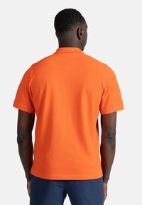 Kraťasová polokošile v jasně oranžové barvě, vyrobená z hladkého bavlněného materiálu. Má klasický límeček a rovný lem. Bez viditelných vzorů nebo akcentů.