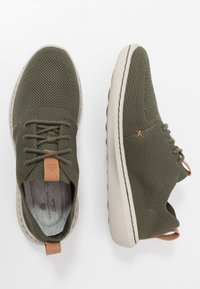 Sneaker knit verde oliva con parte superiore texturizzata, suola in gomma beige, dettagli in pelle marrone e lacci rotondi.