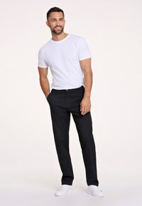 Biała koszulka z krótkim rękawem w połączeniu z ciemnogranatowymi spodniami i białymi trampkami. Slim fit, bez widocznych wzorów czy dodatków. Gładkie tło.