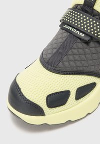 Nærbilde av en gul og svart Jordan-sneaker tå med nettingstoff, lærdetaljer og et belte med Jordan-logoen.
