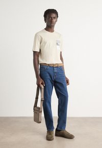 Beige bomull t-skjorte med brystlomme; blå denim jeans; brun belte; grå joggesko; liten lys brun skulderveske med logo.