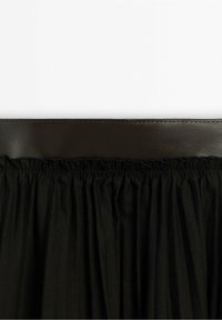 Jupe en tissu noir froncée avec une large ceinture en cuir lisse cousue au bord supérieur.