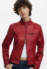 Rote Lederjacke mit Stehkragen, vorderem Reißverschluss und Reißverschlusstasche auf der Brust. Mit glatter Textur und tailliertem Schnitt.