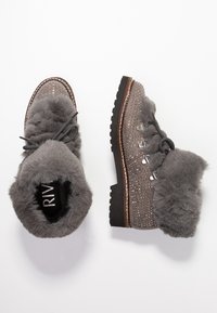 Bottines grises avec doublure en fausse fourrure, design clouté, œillets métalliques et semelle en caoutchouc épaisse. Présente un bout arrondi et un contour contrastant.