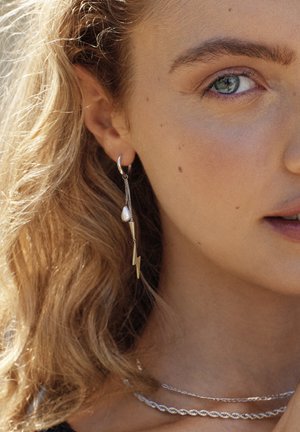 Silberner Creolenohrring mit verlängerter Kette, die eine Perle und ein Blitzdesign aufweist. Glatte Textur, metallischer Glanz und minimalistischer Stil.