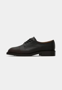 Shoe de couro preto com atacadores, com uma superfície texturada, ponta redonda e costura contrastante; salto plano e acentos de design mínimos.