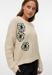 Maglione lavorato a maglia color crema con tre fiori neri ricamati sul lato sinistro, con una vestibilità comoda e polsini a coste.