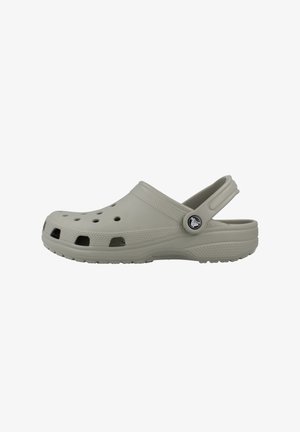 Sabot en caoutchouc gris clair avec des trous de ventilation et une bride de talon réglable ornée d'un bouton rond avec le logo de la marque sur fond blanc.