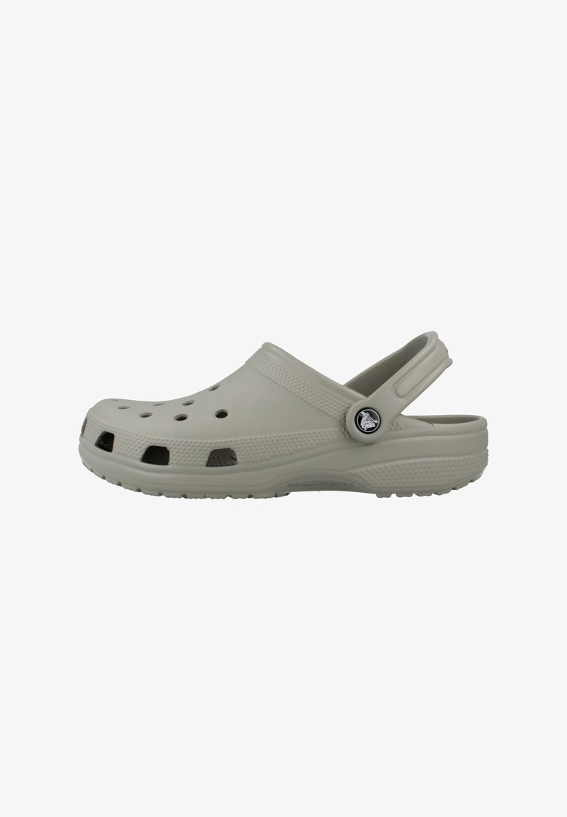 Sabot en caoutchouc gris clair avec des trous de ventilation et une bride de talon réglable ornée d'un bouton rond avec le logo de la marque sur fond blanc.