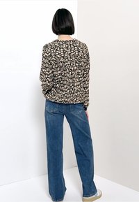 Blouse ample noire avec un motif abstrait beige, associée à un jean en denim bleu taille haute. Design simple, style décontracté.