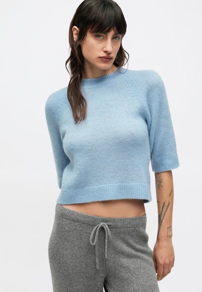 Pulover bleu deschis cropped cu mâneci scurte, tiv striat și textură moale, asortat cu pantaloni gri striați cu talie cu șnur.
