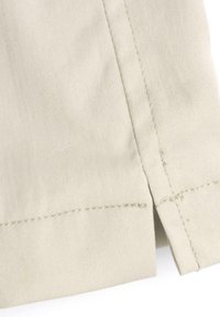 Světlé béžové látky s hladkým povrchem, s pečlivě šitým lemem a bočním rozparkem pro snadný pohyb.