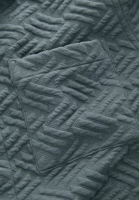 Grau gestepptes Gewebe mit einem strukturierten Zickzackmuster. Weiches Material mit Tiefe, das erhabene Bereiche und eine glatte Oberfläche aufweist.
