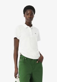 Witte poloshirt van katoen, voorzien van een klassieke kraag, korte mouwen en een groen geborduurd logo op de borst. Gecombineerd met groene broek.